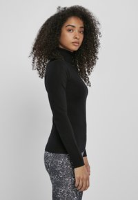 Fekete, testhez simuló garbó pulóver hosszú ujjakkal. Az anyag simának és rugalmasnak tűnik, mintázott leggings-szel párosítva.