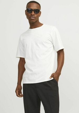 White cotton t-shirt with a crew neckline and short sleeves, paired with black trousers. Smooth texture and simple design, no patterns.