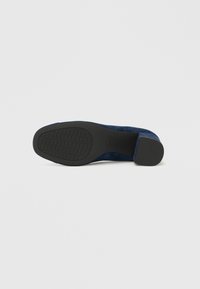 Zapato de tacón alto de ante azul marino con suela de goma texturizada y punta redondeada. El tacón es de forma bloque, proporcionando estabilidad en el diseño.