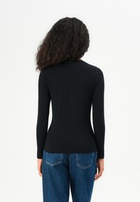 Svart langermet topp laget av glatt stoff, passende silhuett, rund hals, sett fra baksiden, kombinert med høyhårede blå jeans.