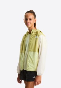 Letvægts to-farvet jakke i sart grøn og creme med hætte, udstyret med fuld lynlås og The North Face-logo på brystet.