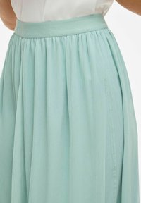 Světle modrá plisovaná sukně s hladkým texturovaným povrchem a širokým pasem, navržená pro volný siluetu.
