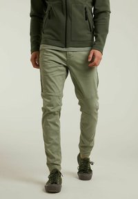 Pantaloni verdi attillati in cotone, con toppe sulle ginocchia, tasche laterali e una consistenza liscia, abbinati a sneaker verdi.