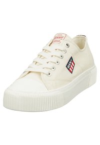 Zapatillas de lona en color blanco roto con suela de goma. Presentan un parche de logo en rojo y azul marino y ojetes metálicos para los cordones. Diseño de punta redonda.