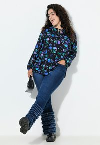 Camicia nera con motivo di teschi colorati, jeans in denim blu e scaldamuscoli blu arricciati. Borsa nera e scarpe nere chunky.