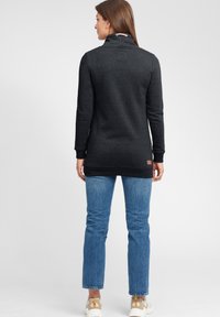 Grå sweatshirt med lång ärm och hög krage, ribbade ärmslut och en texturerad yta. Tillsammans med ljusblå jeans och beige sneakers.
