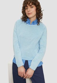 Pull en ribbed bleu clair avec un col rond et des manches longues, porté par-dessus une chemise à boutons bleu clair. S'accorde avec un pantalon noir marine.