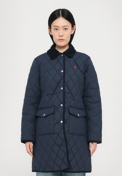 Cappotto trapuntato blu navy con colletto in corduroy, chiusura con bottoni a pressione, due tasche frontali e un piccolo logo rosso sul petto.