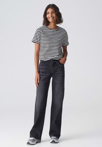 Zwart-wit gestreepte t-shirt met een ronde hals, gecombineerd met hoge donkere jeans met een koord. Draagt grijze sneakers.