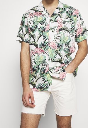 Kurzärmliges Hemd mit einem weißen Hintergrund, das ein farbenfrohes tropisches Muster aus rosa Flamingos und grünen Palmenblättern zeigt.