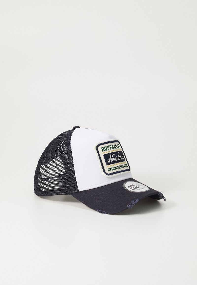Gorra de camionero con parte frontal blanca, visera azul marino y parte trasera de malla negra. Presenta un parche rectangular con el logotipo y detalles de costura en la visera.