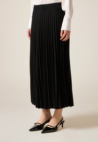 Musta laskostettu midihame, kevyt kangas ja istuva vyötärönauha. Yhdistetty kiiltävän mustiin teräväkärkisiin slingback-korkoihin.