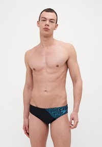 Fatos de banho pretos com riscas diagonais azuis. Feitos de material elástico, com um logótipo na cintura. Design suave e ajustado.