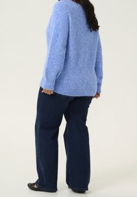 Pull en maille douce bleu clair avec une coupe ample et un ourlet côtelé, associé à un jean large bleu foncé et des ballerines noires.