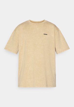 Beige Übergröße T-Shirt mit weichem Material, kurzen Ärmeln und Rundhalsausschnitt. Mit einem kleinen schwarzen Etikett auf der Brust, das den Markennamen zeigt.