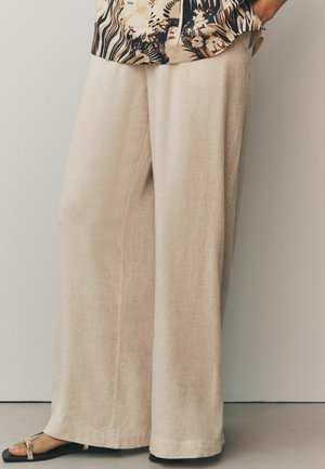 Beige vida linbyxor med en texturerad yta, med skräddarsydd skärning och rak fåll, tillsammans med svarta sandaler.