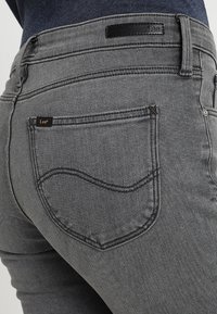 Vaqueros de mezclilla gris con un corte slim, que presentan un diseño de bolsillos traseros curvados y una pequeña etiqueta de la marca en la cinturilla.