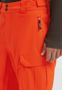Oranje cargobroek van duurzaam materiaal, met een ritszak en een klepzak, met een vlak ontwerp aan de voor- en achterkant.