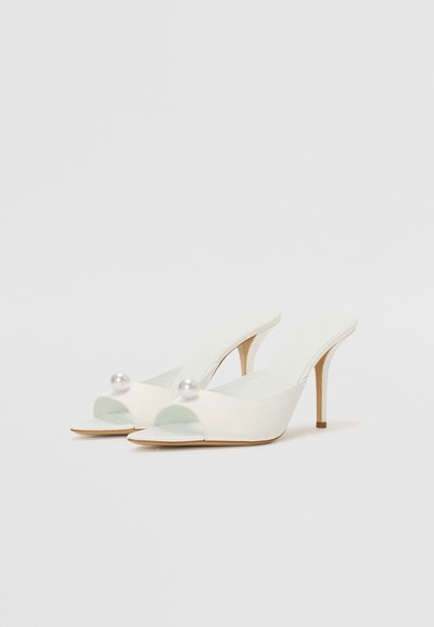 Pump in bianco con punta aperta e cinturino slingback, dal finish lucido e decorati con perle sulla punta, con tacco a stiletto sottile. Design minimalista.
