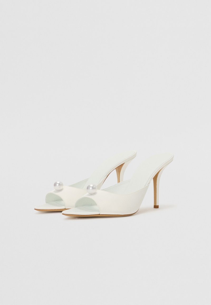 Hvide åbne slingback hæle med højglans finish, der har perleaccentueringer ved tæerne og en slank stiletto hæl. Minimalistisk design.
