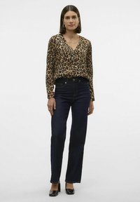 Blusa a maniche lunghe con stampa leopardata e scollatura a V, abbinata a jeans in denim scuro a vita alta e scarpe con tacco a blocco nere.