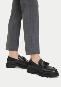 Čierne kožené loafers s hrubou podrážkou, ozdobené třásňami a zlatými prvkami, textúrovaným šitím a hladkým povrchom.