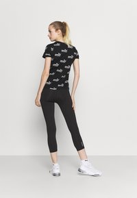 T-shirt aderente nero con motivi grafici bianchi ripetuti, abbinato a leggings neri e scarpe sportive bianche con accenti argento.