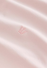 Tissu rose doux avec un petit symbole de couronne brodé en fil rose assorti, centré sur un matériau légèrement ondulé.