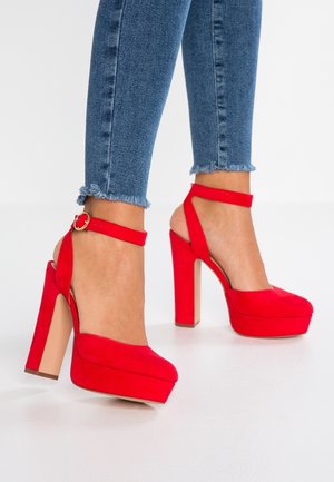 Rode suède hoge hakken met platform, een dikke hak en een enkelbandje. Glad voorwerp en rond te ontwerp.