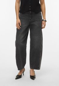 Jeans neri a vita alta con una vestibilità larga e morbida, caratterizzati da una texture sbiadita. Presentano tasche frontali e un orlo dritto, abbinati a scarpe nere con tacco.