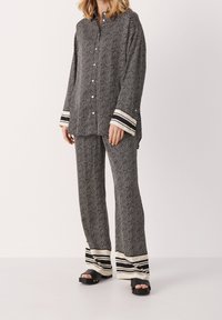 Ensemble chemise et pantalon à motif chevron noir et blanc, avec des poignets rayés et une coupe décontractée. Le tissu semble doux et texturé.