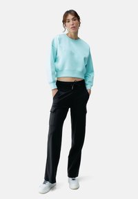 Mintgroene cropped sweatshirt met een ronde hals, gecombineerd met zwarte cargo broeken met zijzakken. Model staat in witte sneakers.