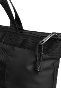 Czarna torba nylonowa z fakturowanym materiałem, dwoma górnymi uchwytami oraz srebrnym zamkiem błyskawicznym z sznurkiem do bezpiecznego zapięcia.