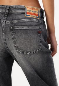 Dark grey denim jeans with faded areas, five-pocket design, and a distinctive leather patch tag at the waistband featuring brand details.