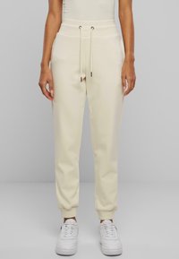 Joggers de color crema con un acabado texturizado, cinturilla elástica con cordones y puños ajustados. Combinados con zapatillas blancas.