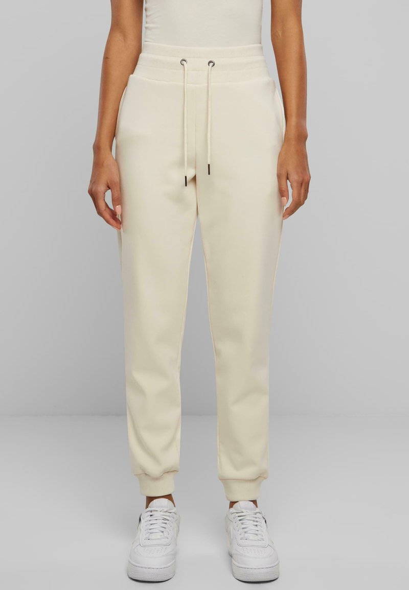 Joggers de color crema con un acabado texturizado, cinturilla elástica con cordones y puños ajustados. Combinados con zapatillas blancas.