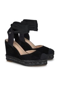 Sandali con zeppa nera, in suede, con punta intrecciata. Presentano una piattaforma texturizzata decorata con dettagli in perline e un laccio incrociato alla caviglia.