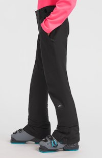 Zwarte snowboardbroek met een gladde textuur en versterkte stiksels. Voorzien van zijzakken en een logo-patch. Gecombineerd met grijze skibotten.