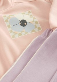 Jasnoróżowy sweter z grafiką kwiatu w niebieskim, czarnym i brzoskwiniowym kolorze na kratkowanej łatce; w komplecie z miękkimi lawendowymi spodniami dresowymi.