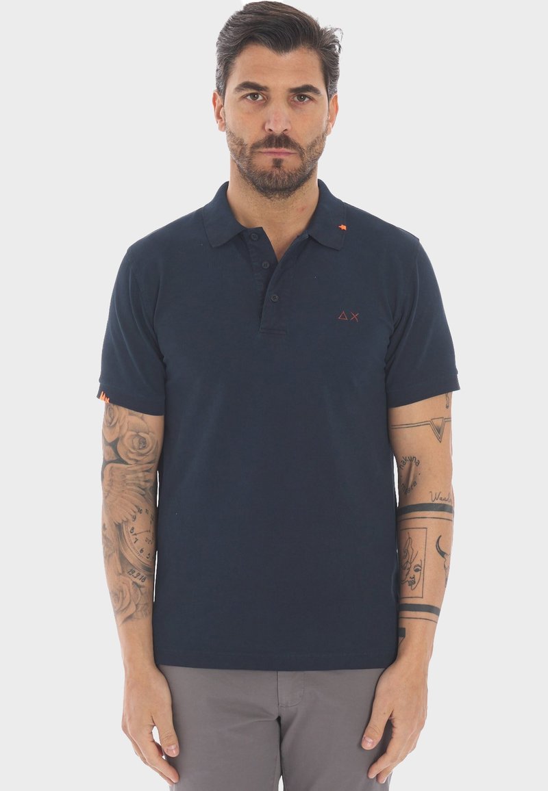 Polo blu navy in cotone, con colletto a due bottoni, maniche corte e un dettaglio del logo arancione sul lato sinistro del petto.