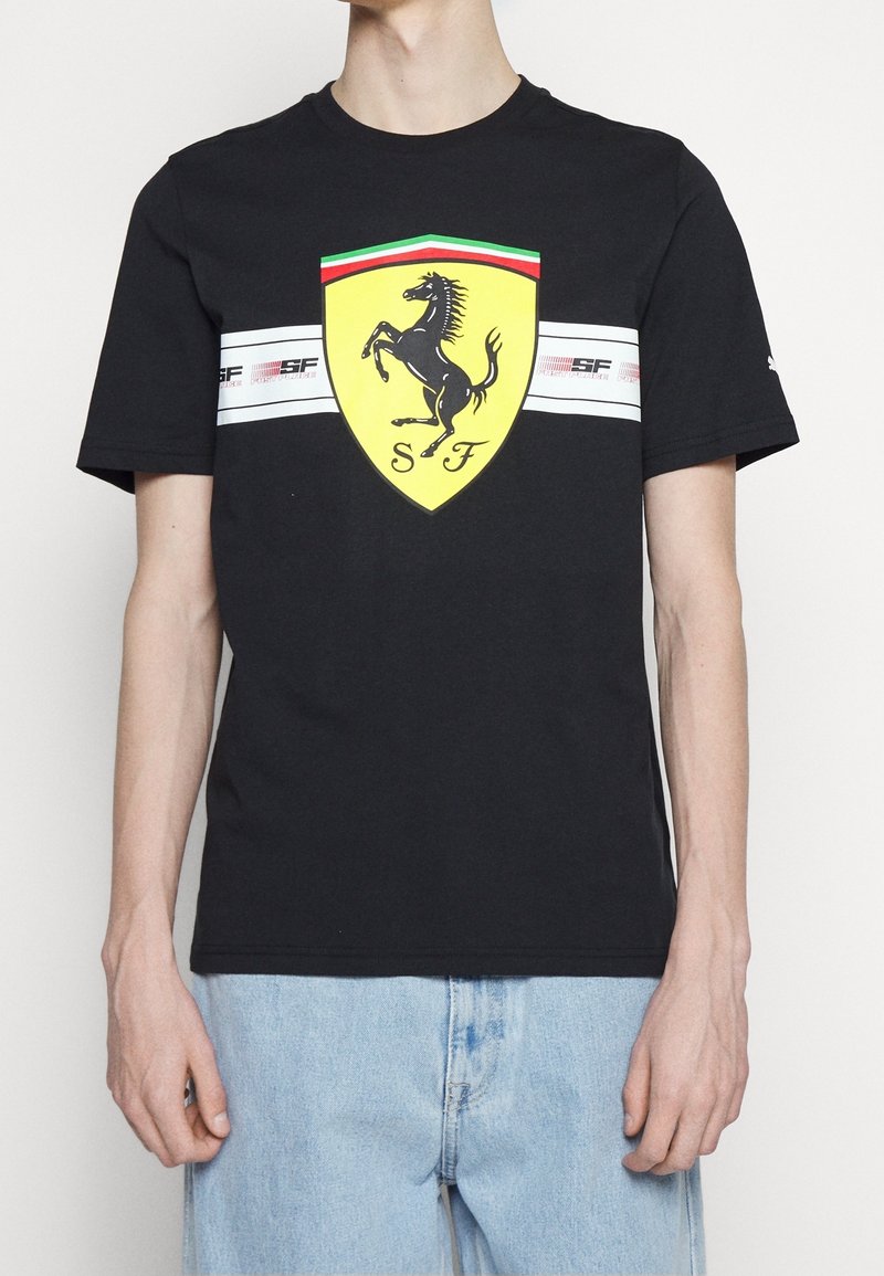 Svart bomull t-shirt med en gul Ferrari-logotyp och en prancing horse-design. Har vita horisontella ränder med röda och gröna detaljer.