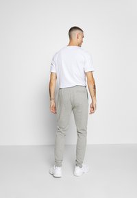 Grå sweatpants med en tætsiddende ben, elastiske manchetter og baglomme, parret med en hvid t-shirt med korte ærmer, set fra bagved.