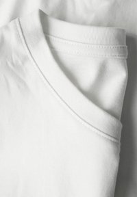 Κοντινό πλάνο λευκού βαμβακερού T-shirt διπλωμένου, εστιάζοντας στο ραμμένο στρογγυλό λαιμόκομμα και την απαλή υφή του υφάσματος.