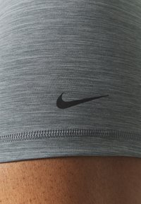 Szary materiał sportowy z teksturowanym wzorem, z czarnym logo Nike. Brzeg ma gładkie, przeszyte wykończenie.