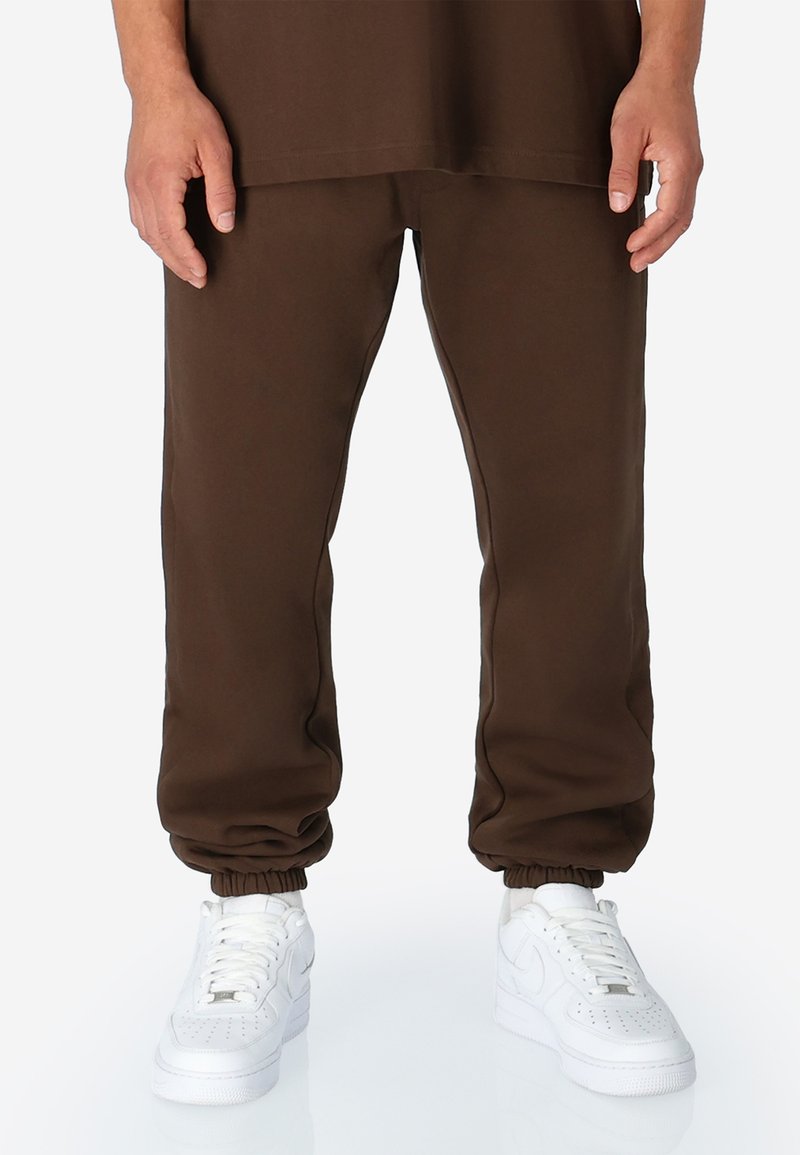 Bruine joggingbroek met elastische manchetten, gemaakt van zachte stof. Gecombineerd met witte sneakers met geperforeerde accenten en platte veters.