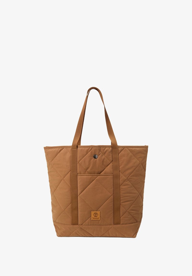 Sac cabas matelassé marron avec deux longues poignées, poche avant pressionnée et écusson logo Timberland sur fond blanc uni.