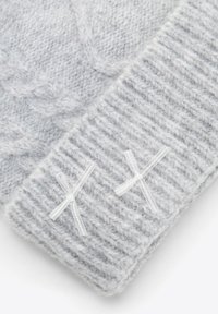 Jasnoszara dziana czapka z wzorem warkocza, prążkowanym brzegiem i dwoma białymi wstążkami jako ozdobą. Miękki i teksturowany materiał.