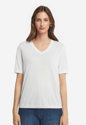 Vit V-ringad T-shirt med korta ärmar, slät bomullstyg, avslappnad passform och ribbat kantband vid halslinningen och ärmarna. Bärs med blå jeans.
