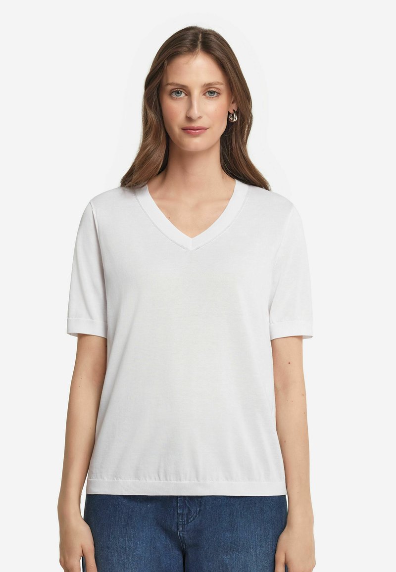 Hvid V-hals T-shirt med korte ærmer, glat bomuldsstof, afslappet pasform og ribbet kant ved halsudskæringen og ærmerne. Bæres med blå jeans.
