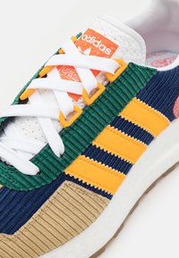 Adidas Sneaker mit einer Mischung aus grünem, blauem, orangefarbenem und tanfarbenem geripptem Cordmaterial sowie glatten Materialien, weißen Schnürsenkeln und strukturierten Sohlen.